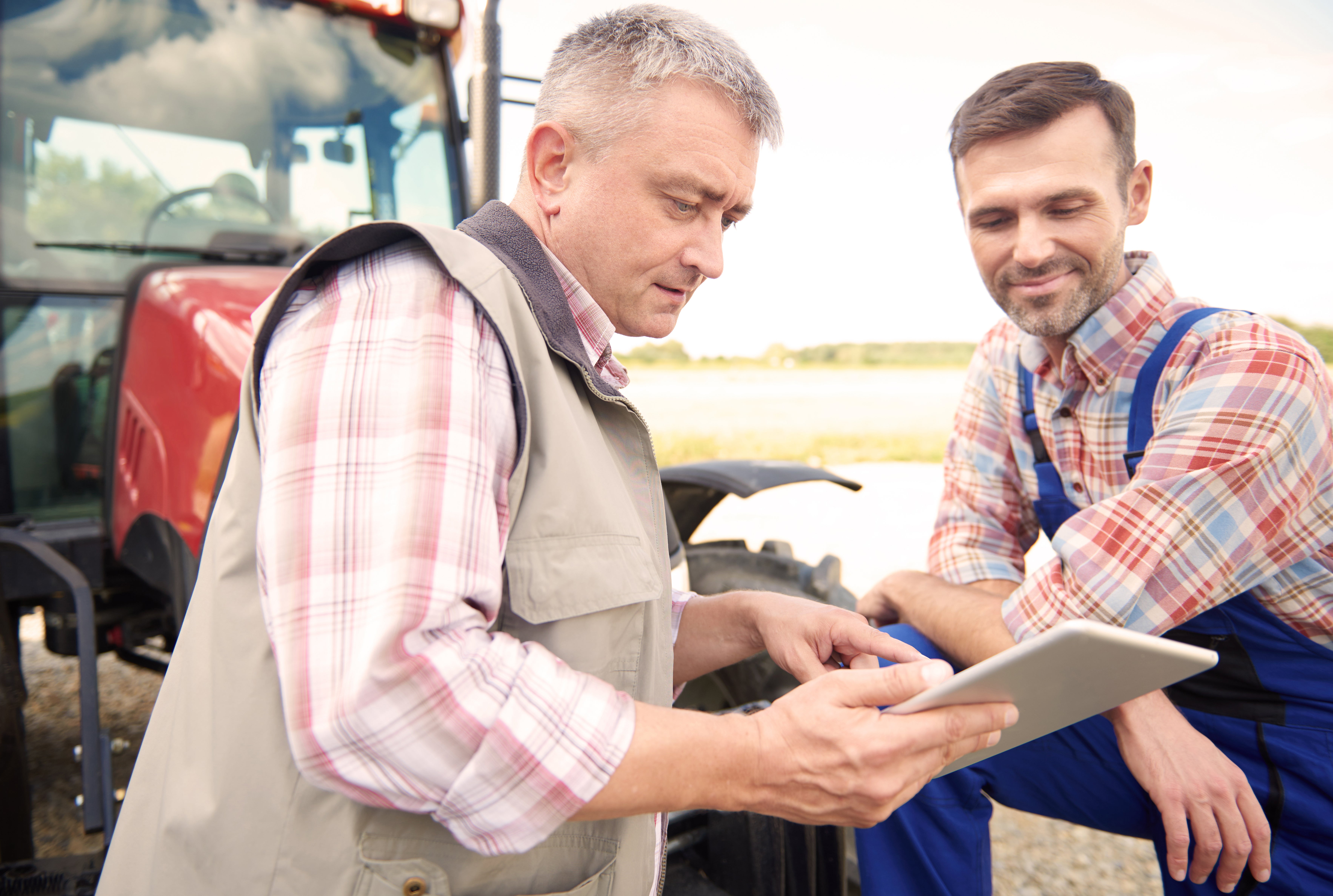 Farmers leaning on a red tractor while looking at a tablet.